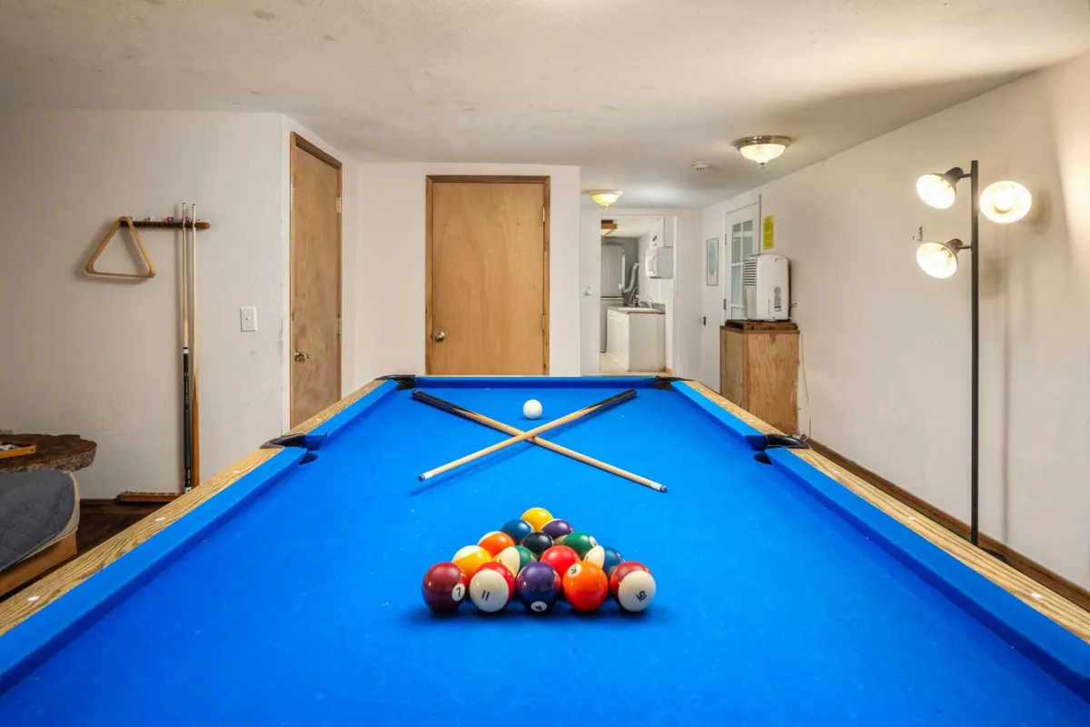 An inviting game room interior featuring a pool table with colorful balls, ambient lighting fixtures, and a playful, lively mood. The arrangement implies the perfect setting for friendly competitions and social gatherings after a day out.