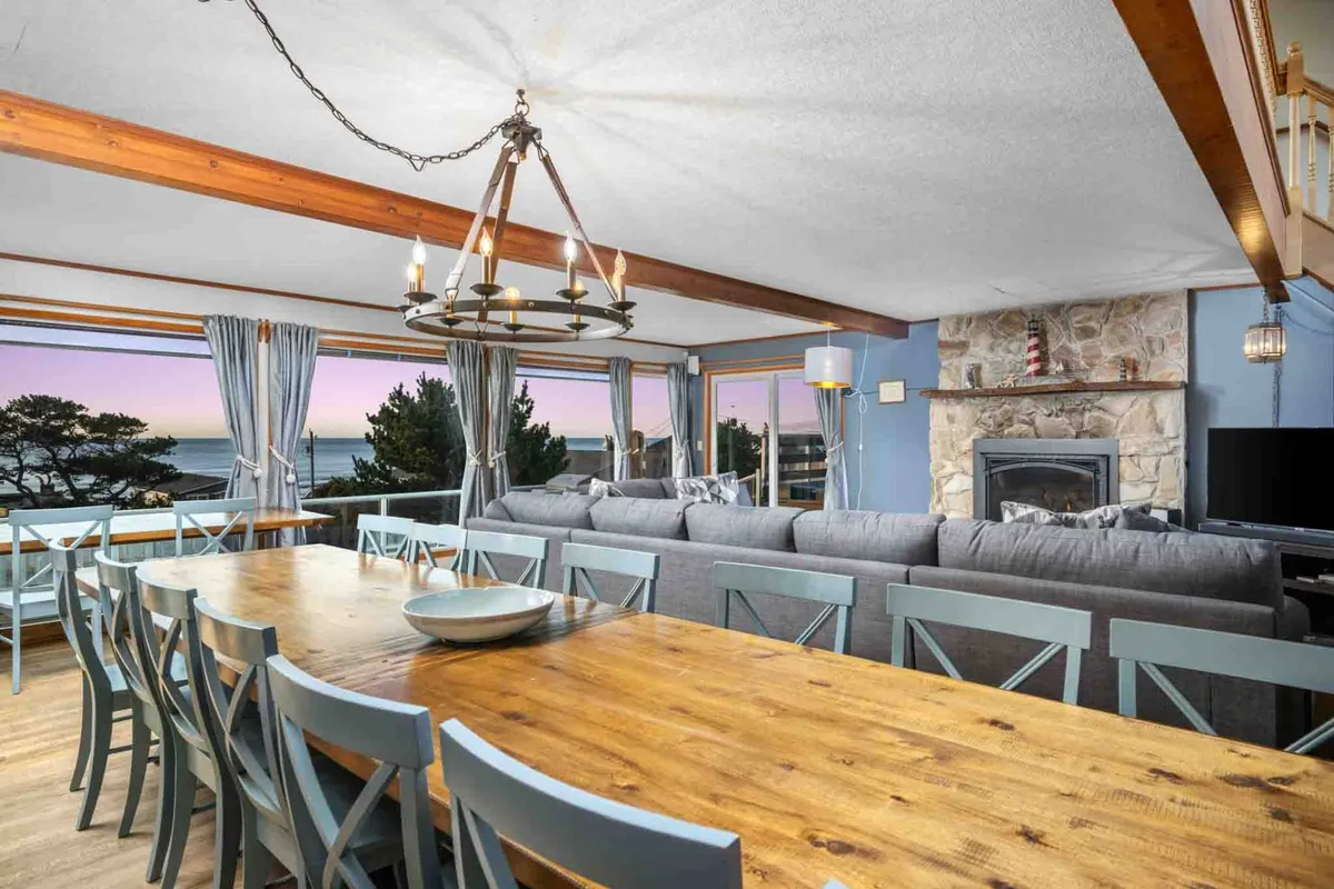 An inviting interior with a cozy sofa and a dining table set beside large windows that frame the ocean view. The fireplace creates a warm, welcoming atmosphere, perfect for both relaxation and shared meals, with natural light pouring in from the windows.