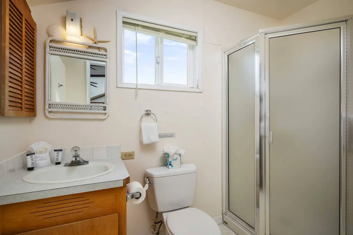 A fresh and functional bathroom with a vanity sink, a shower stall, mirror, and a window letting in daylight. The clean design and modern features promise comfort and privacy for guests.