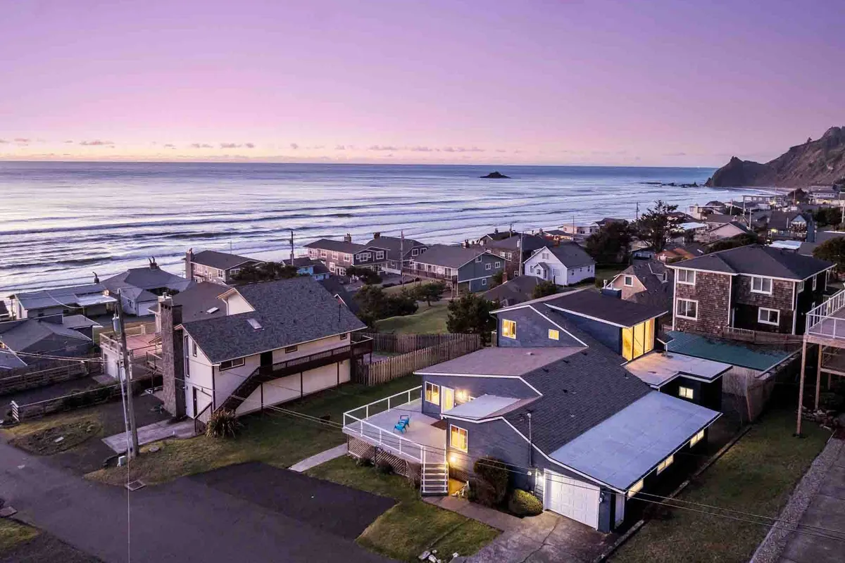 This image captures a sweeping view of the coastline at sunset, with gentle waves rolling in, a vibrant sky, and nearby houses nestled on the hillside. The scene evokes relaxation and the inviting natural beauty that defines a Lincoln City beach excursion.